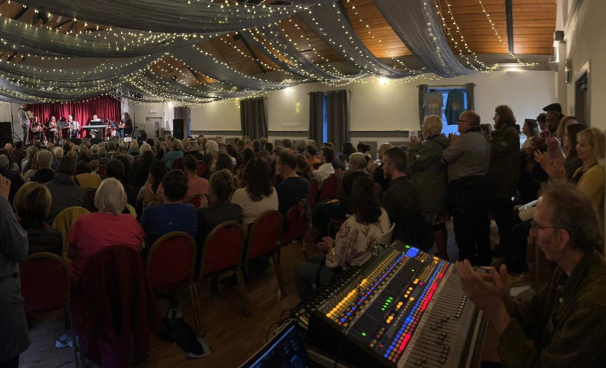One of the Fiddle Week Concerts in full swing, viewed from the back, with fairy lights and drapes across the top of the hall