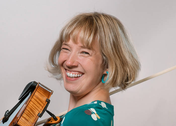 Patters, smiling with her head turned to the camera and fiddle and bow in hand
