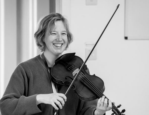 Patters, smiling with her head turned to the camera and fiddle and bow in hand