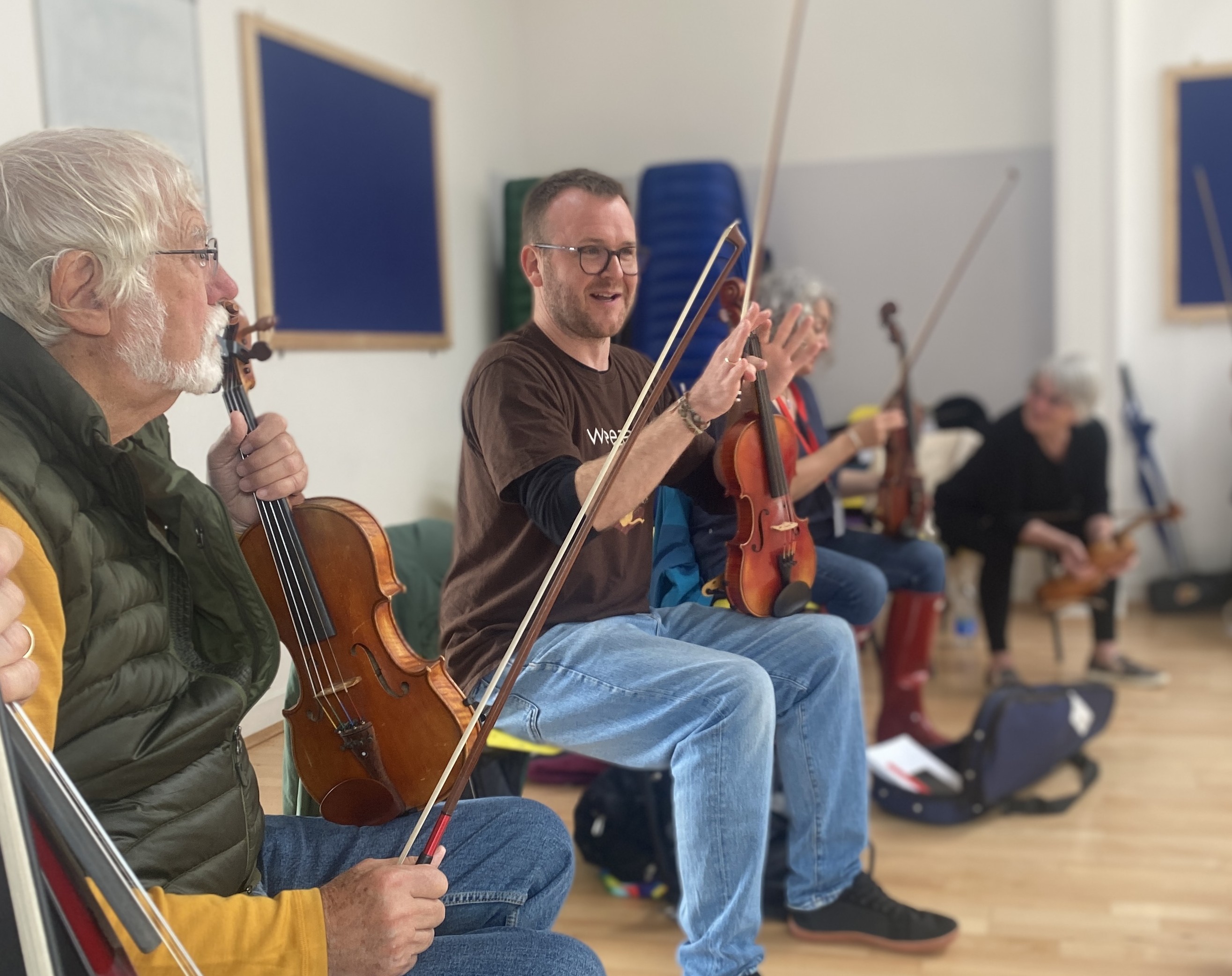 Sam, sat on a chair in class holding his fiddle surrounded by attentive learners as he explains something